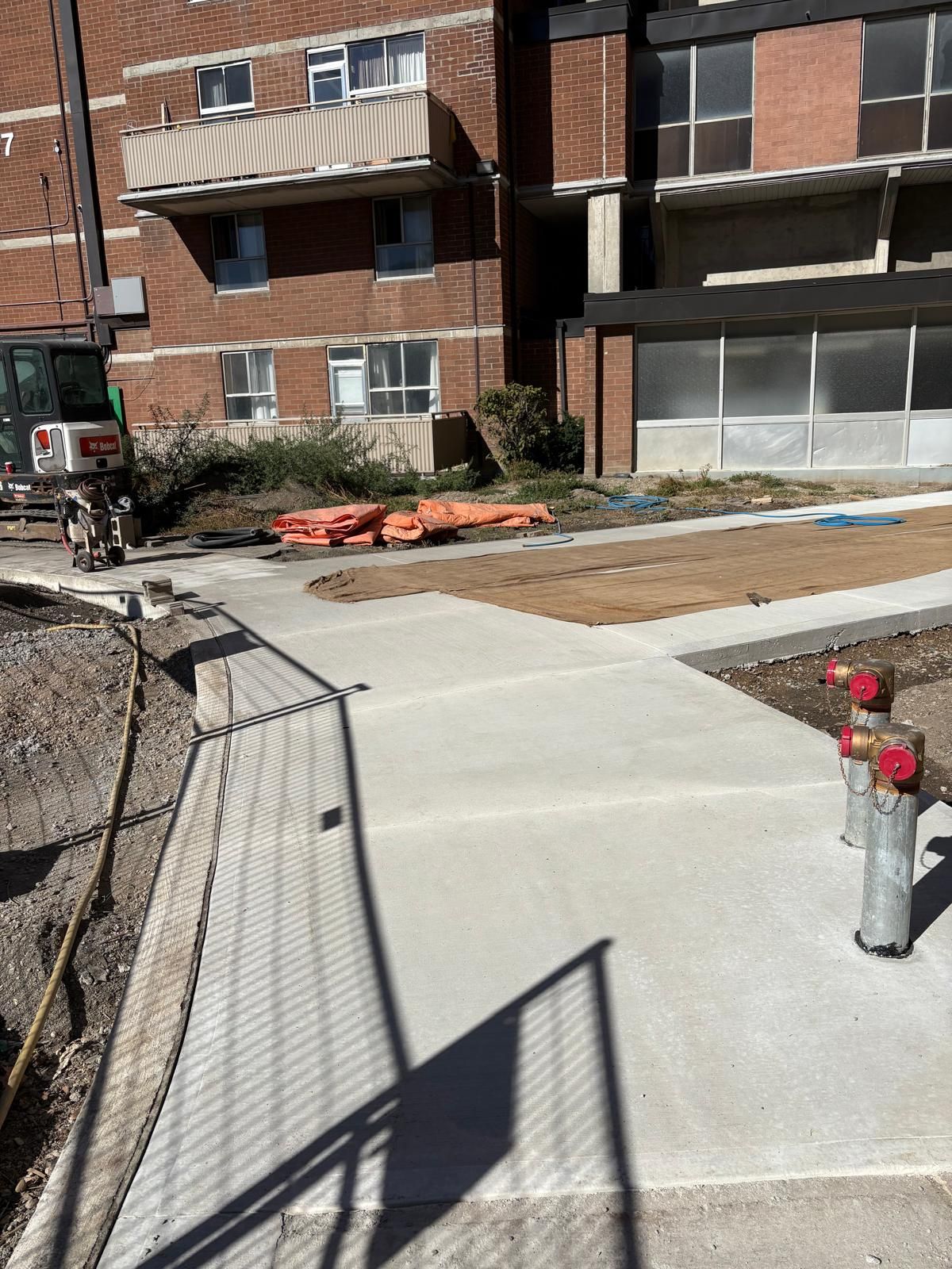 Finished concrete sidewalk beside an excavator at a Homecrete jobsite